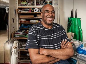 A photo portrait of Horace from the waist up. He has his arms crossed and a big smile on his face. He is in the Venture Arts studio with art materials behind him.