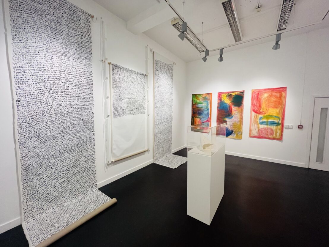 A large white room with colourful artworks on one wall, black and white text artworks on the other wall