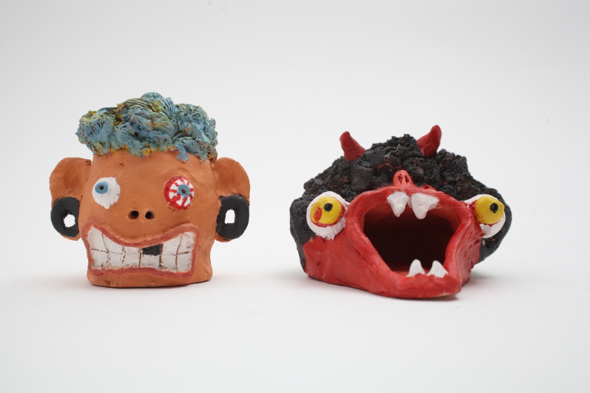 Two clay heads painted orange and red, with silly, monster like faces.