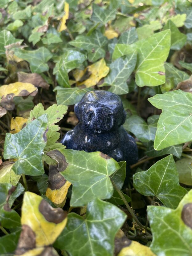 Dark clay figure peeping out from under green ivy leaves