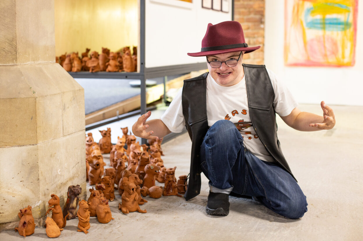 Artist Dominic Bennett knelt on the floor in front of his ceramic weasel army.