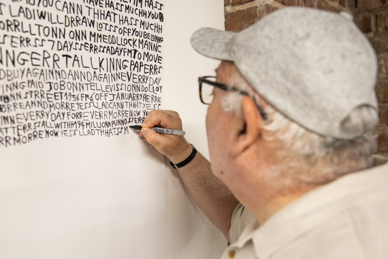 Artist Barry Finan with a black pen on a white scroll.