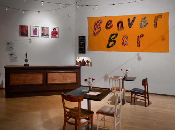 The Beaver Bar at the Julie Party - a bar, table and chairs are set out in a room, a large fabric banner with 'Beaver Bar' is on the other wall.