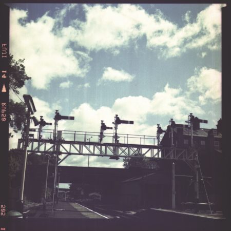Aged or old photograph of a train station platform and signals, a blue sky with white clouds.