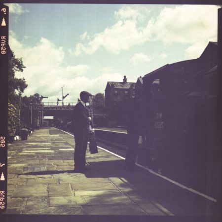 Aged or old photograph of man dressed smartly, standing at train station