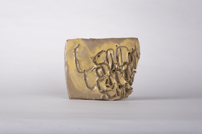 Ceramic sculpture, grey and gold colours, with receptive text pattern cut into it.