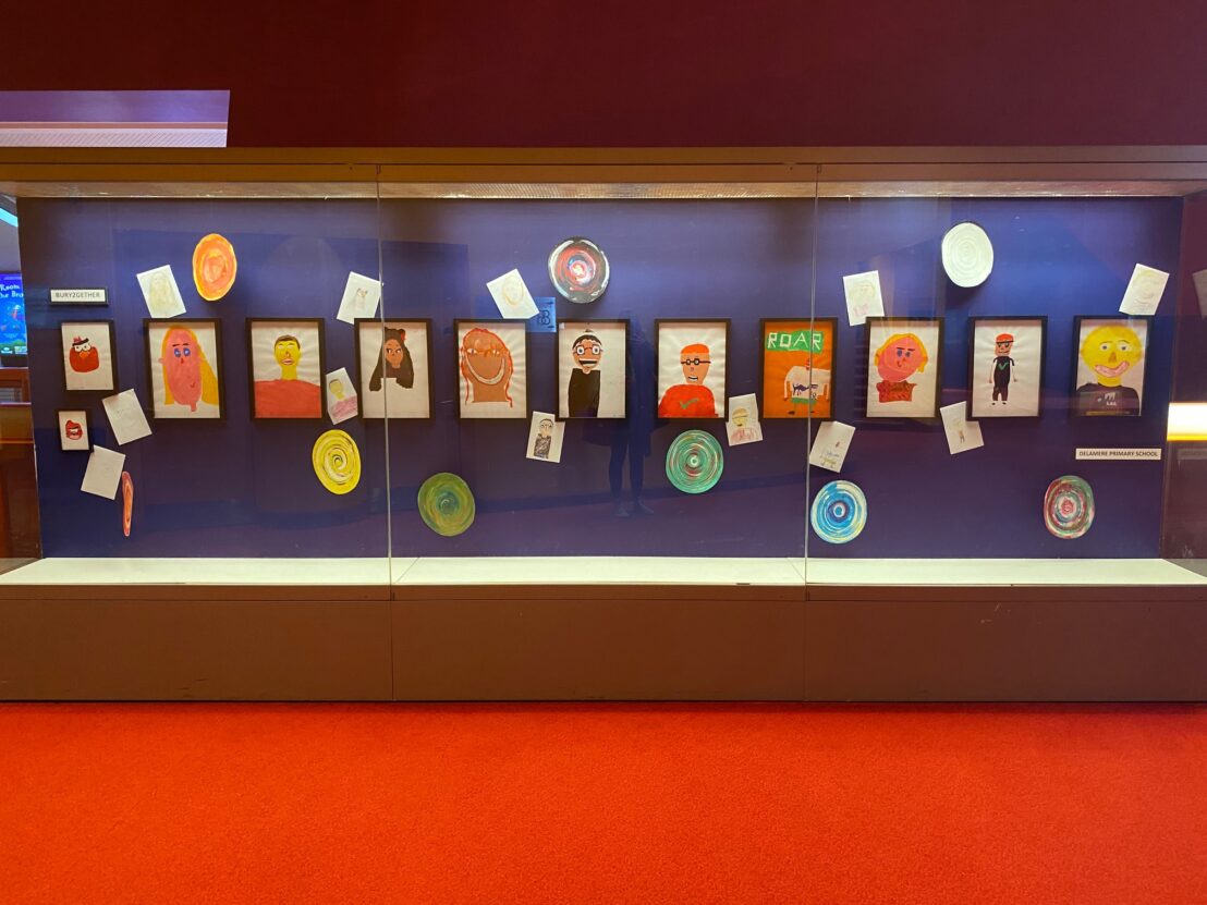An exhibition case at The Lowry showing a number of portraits created during schools projects.