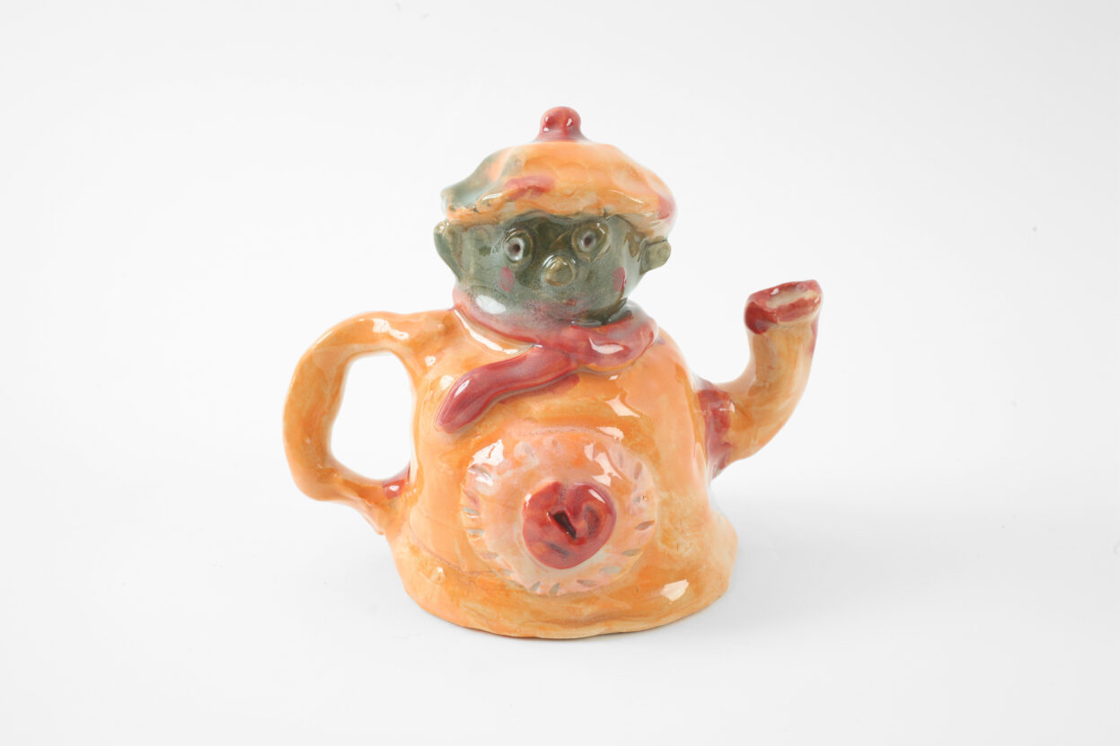 A ceramic orange watering can with a face and hat, by Louise Hewitt