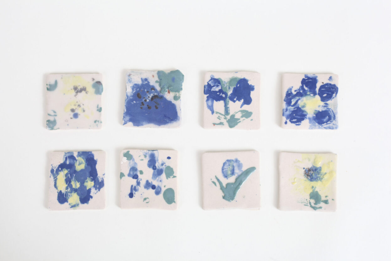Eight small square ceramic tiles with blue, green and yellow floral patterns, by Sarah Lee