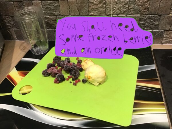 Image from Liam Ashworths's smoothie cookbook, showing fruit on a green chopping board. Text in a purple box reads 'you shall need some frozen berries and an orange'