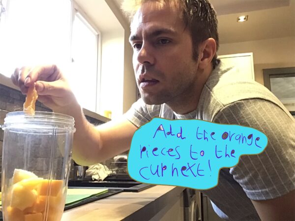 Image from Liam Ashworth's smoothie cookbook - the photo shows Liam adding fruit to a blender. Text is in a blue box which reads 'add the orange pieces to the cup next!'