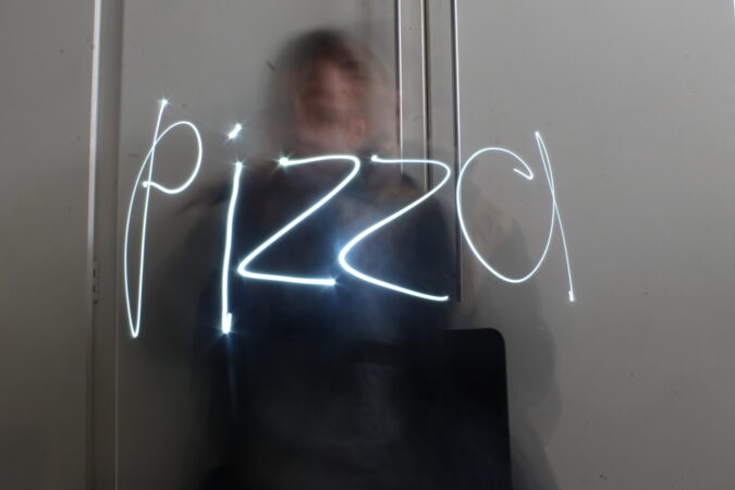 A blurry photo of a man taken in a mirror, with the word 'pizza' written over the image, by Liam Ashworth