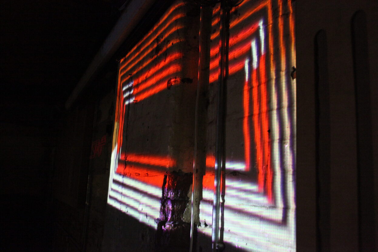 Red and white lights in a square shape, projected onto a dark wall - projection mapping by Malik Jama