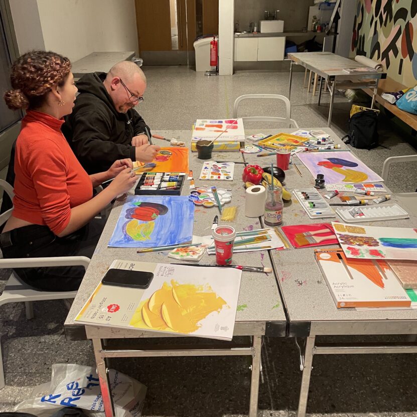 Two artists sat at a table covered in art materials.
