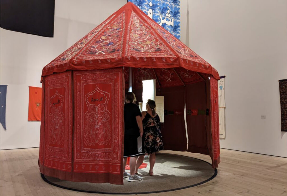 A big room containing a large red embroidered tent, two people standing inside it