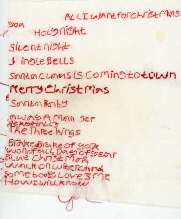 Textile Arts on a cream fabric. Red thread used to make words. Words list famous Christmas songs.