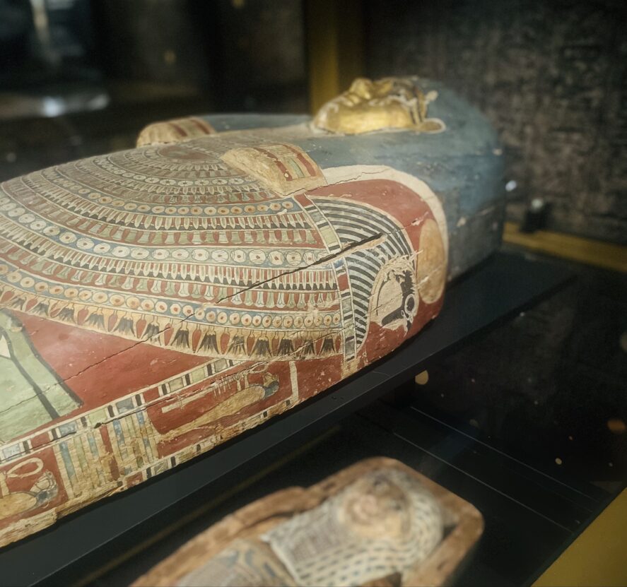 Two painted wooden Egyptian coffins in a glass case.