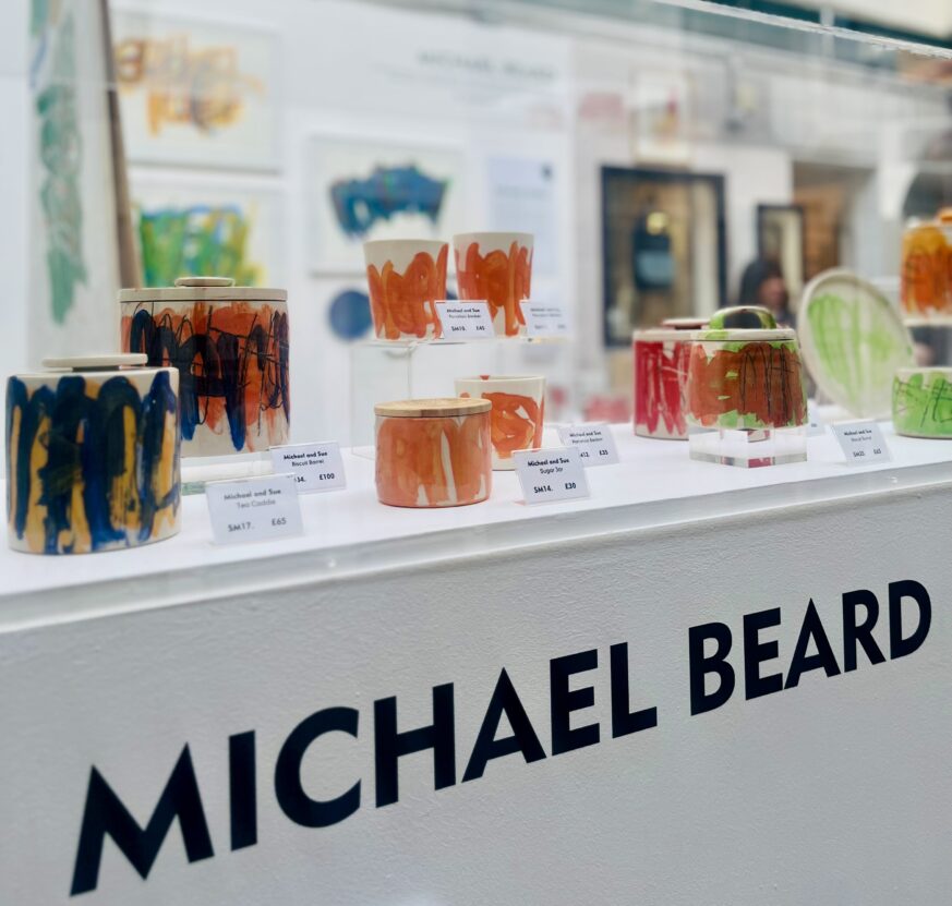 A glass cabinet displaying colourful ceramics with the words 'Michael Beard' written on the front.