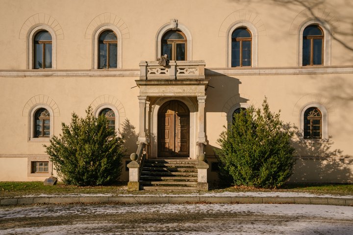 The front door of an old palace with cream walls and a cross above the door.
