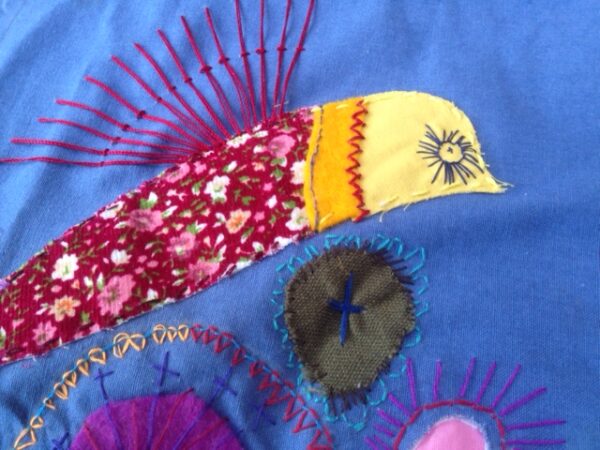Close up of textile art of a bird made with appliqué and embroidery. Main colour is blue.