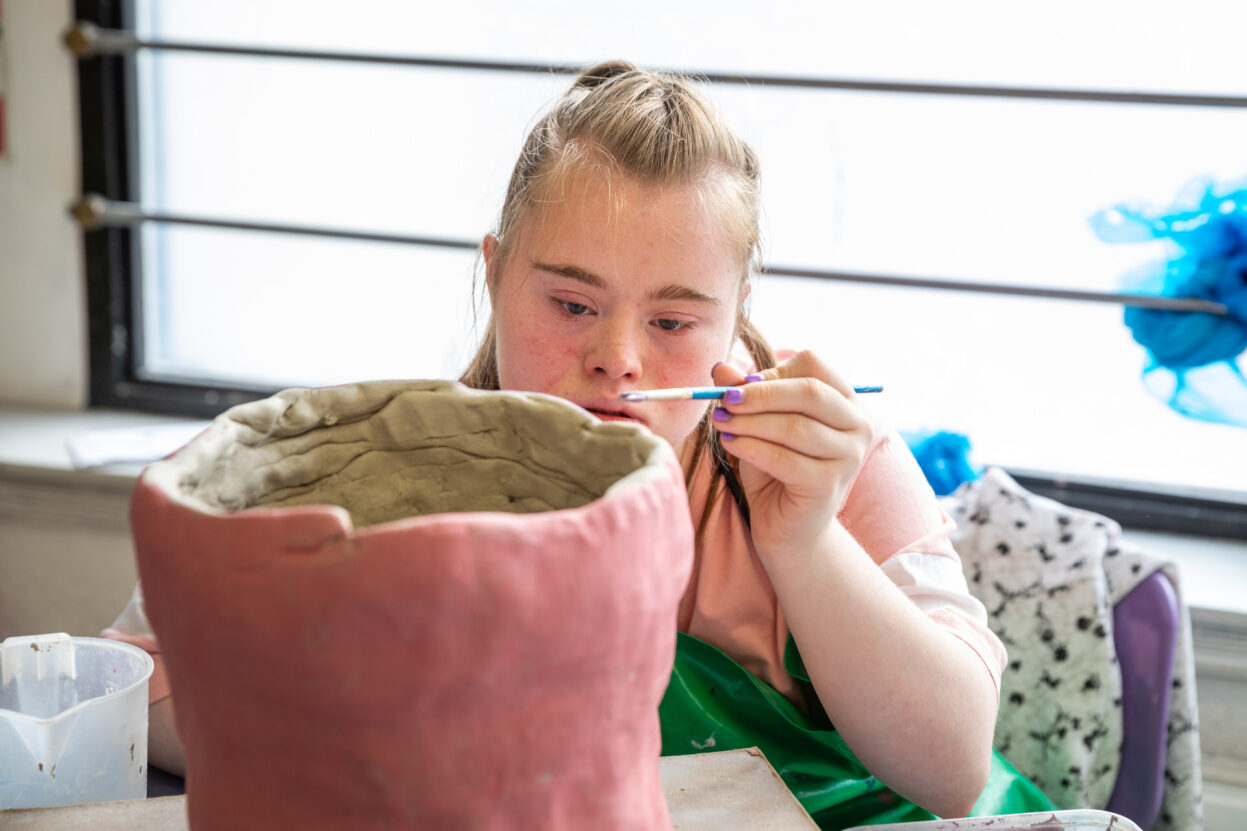 Young girl painting a clay pot with pink paint.