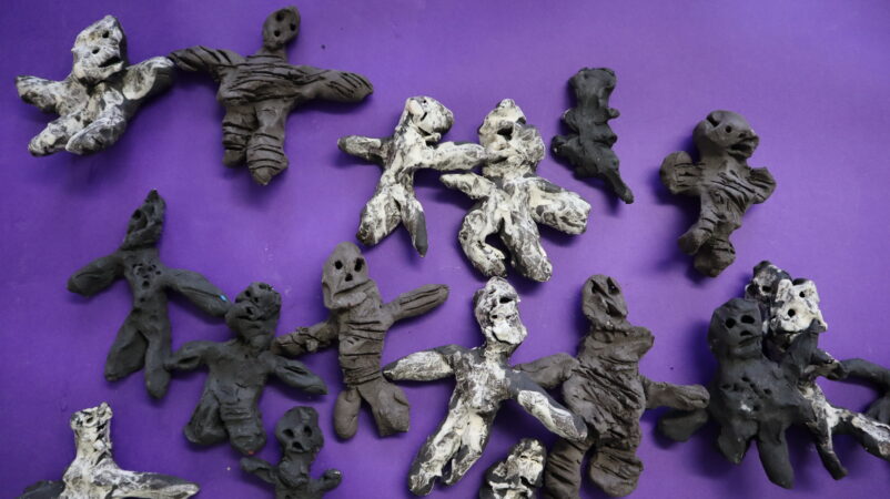 A selection of human like figures made of clay, in a variety of grey colours.