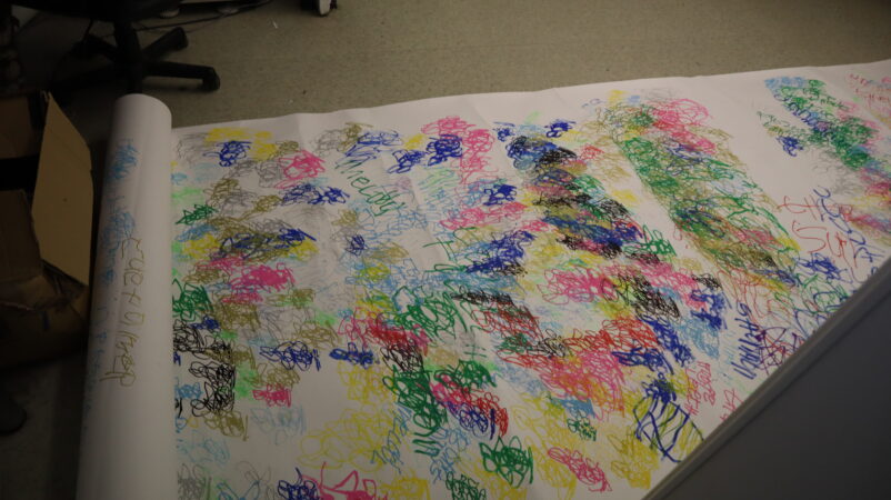 Large roll of paper lay on the floor, unravelled showing multicoloured abstract art