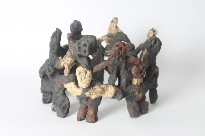 Ceramic sculpture of a group of human-like figures standing and linked together in a circle.