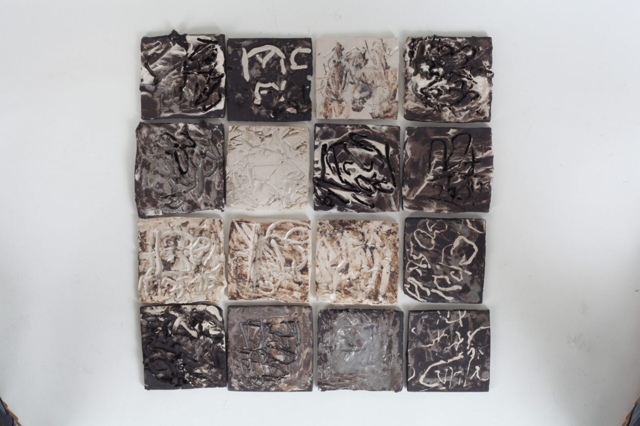 16 square ceramic tiles, cream, greys and black. Edged into to create texture.