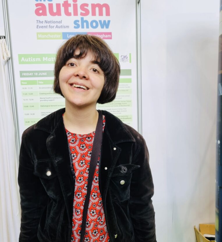 Young woman smiling stood in front of a banner saying autism show.