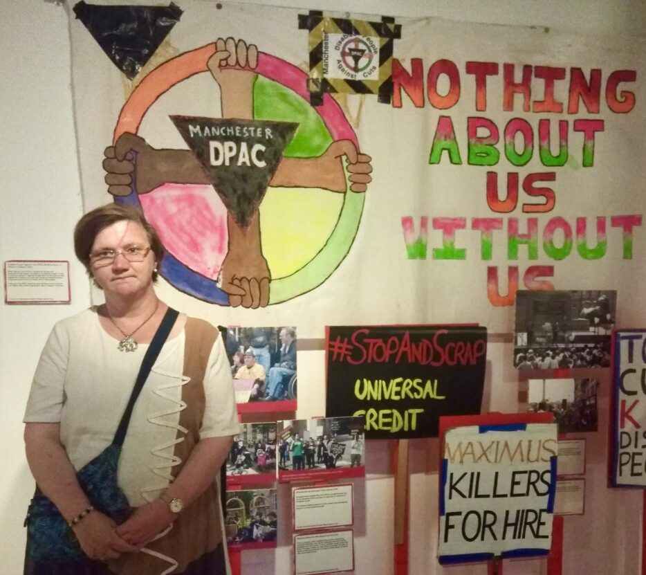Louise Hewitt stood in front of protest banners at Nothing about us without us exhibition