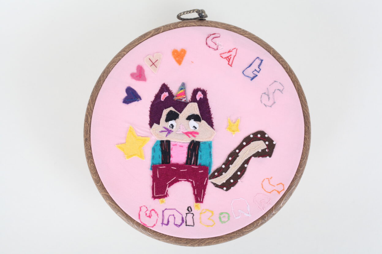 I circular piece of embroidery of a cat unicorn with the words 'cats unicorns' embroidery above.