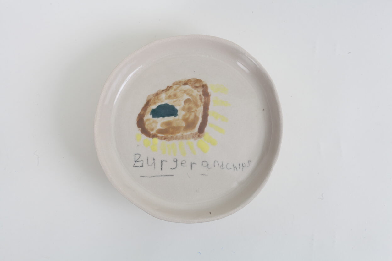 Round, white ceramic plate painted with a picture of food and the words 'burger and chips'.