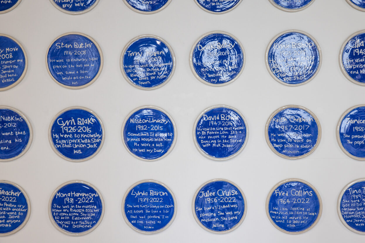 A selection of ceramic blue plaques presented on a white gallery wall.