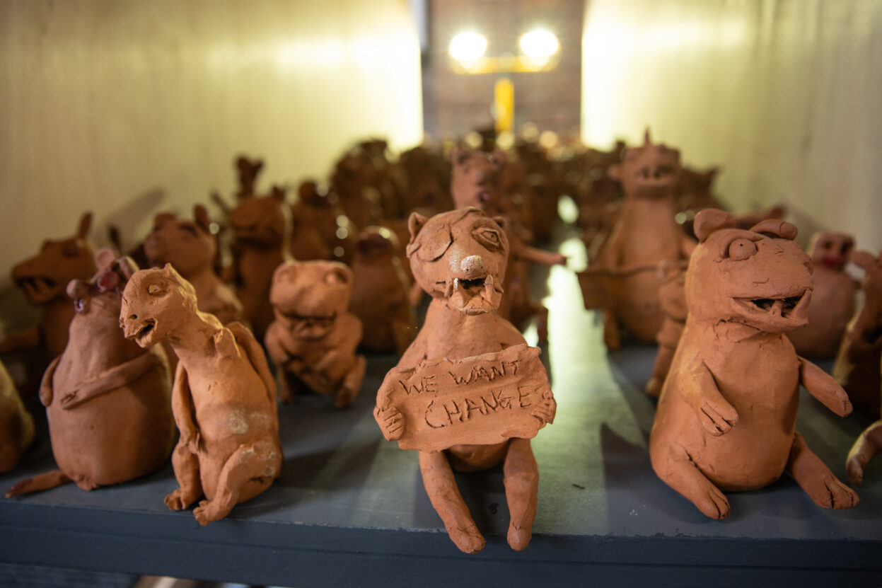 A large number of small ceramic weasels about 8cm high. The front one is holding a banner say 'we want change'.