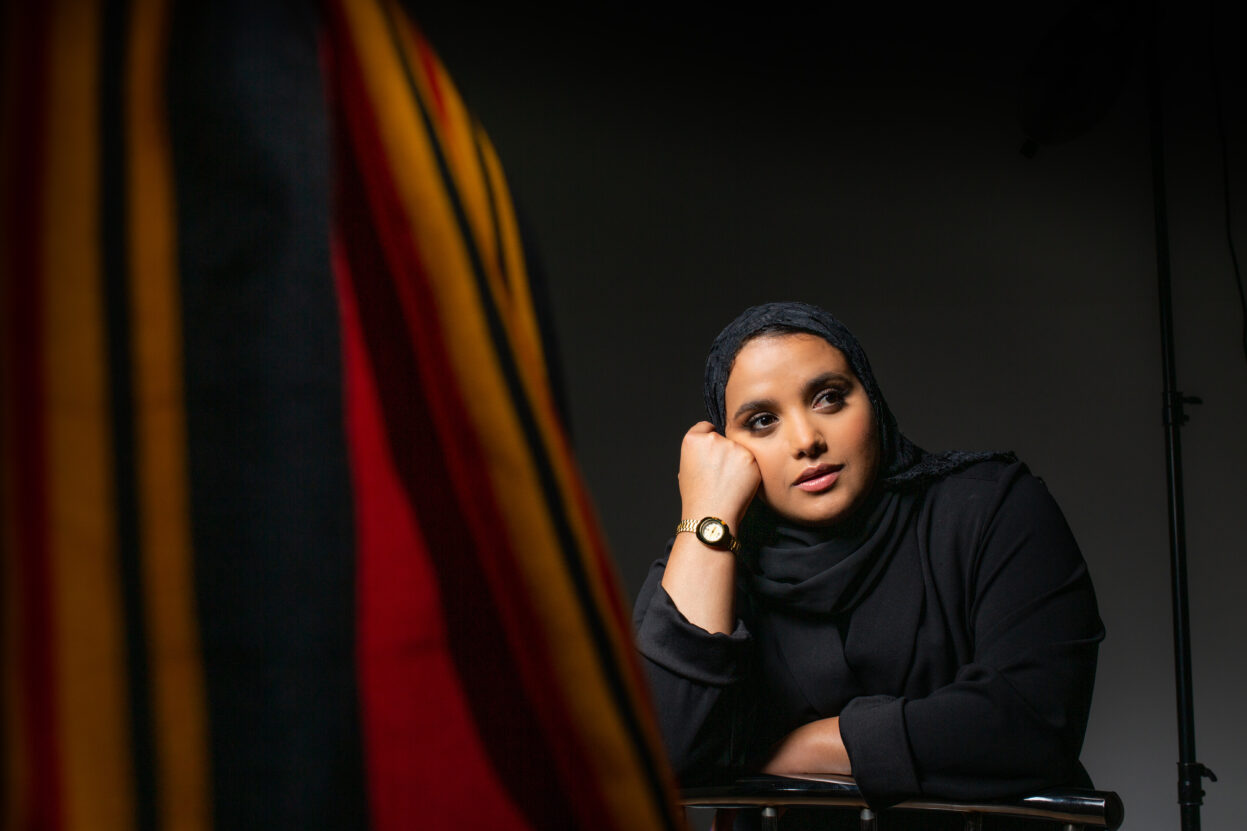 A woman wearing all black with her face leaning against her hand, with a black background.