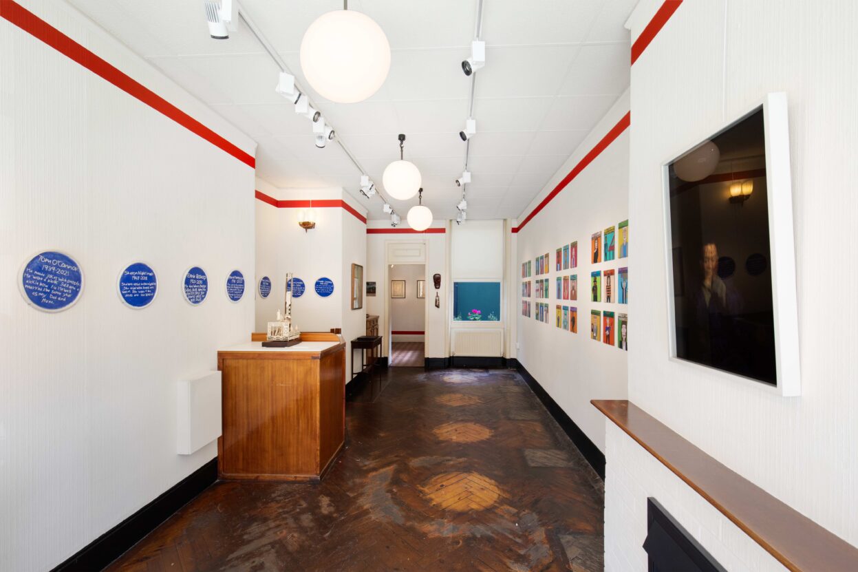 A gallery room with white walls, a wooden floor and various artworks on the walls.