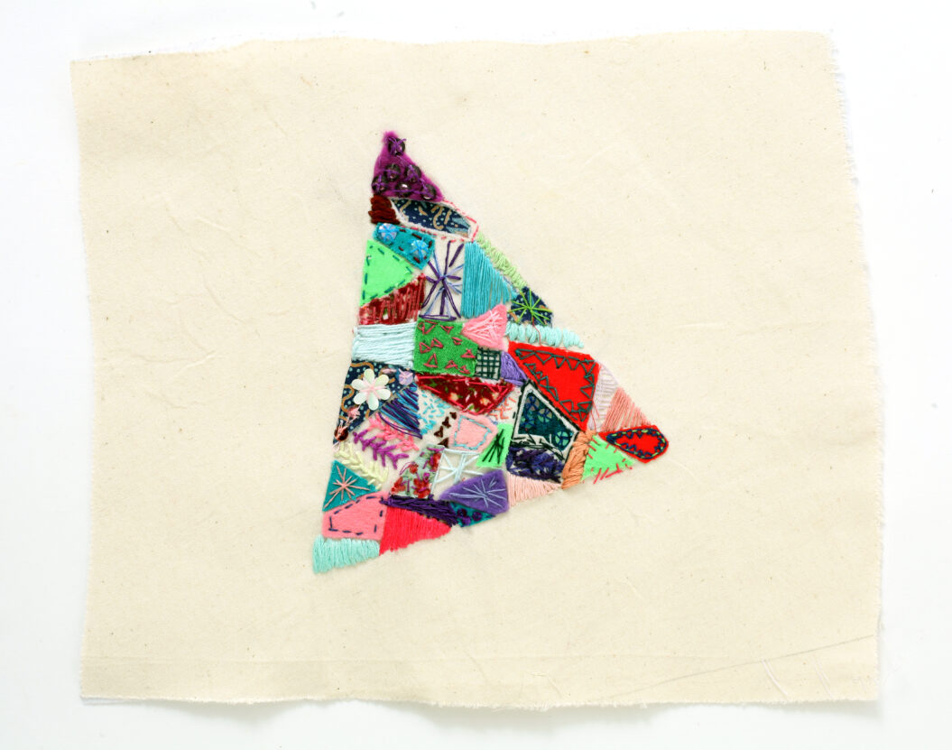 Embroidered piece if textile art, a colourful triangle made up of lots of pieces of material.