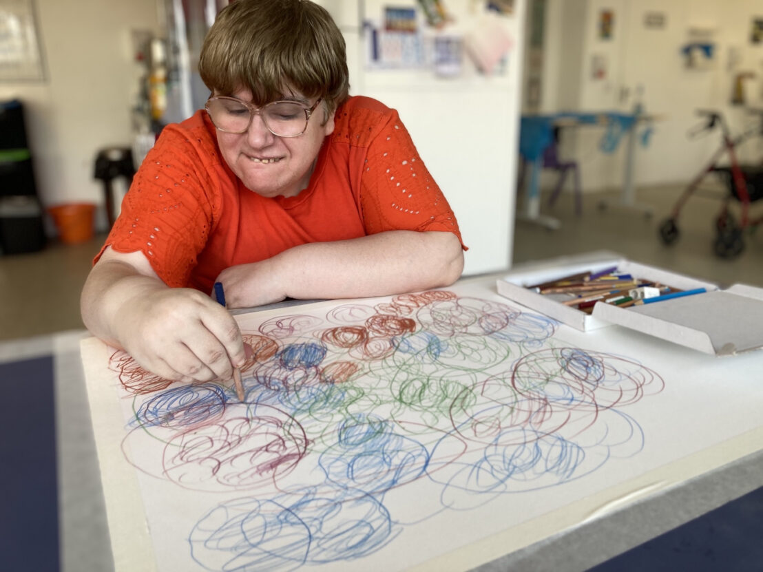 Artist Kathy Wilmott sat at a table drawing on a large piece of white paper.