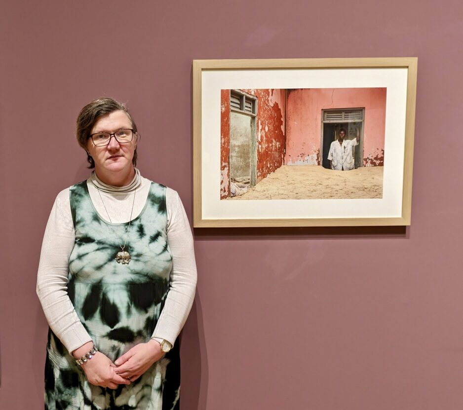 Louise Hewitt stood in front of a framed artwork on a purple gallery wall.