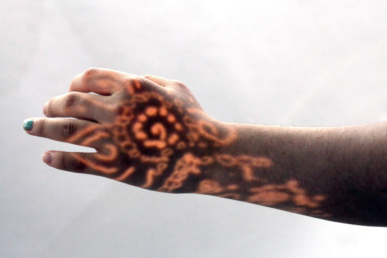 A hand and wrist with henna designs projected on with light.
