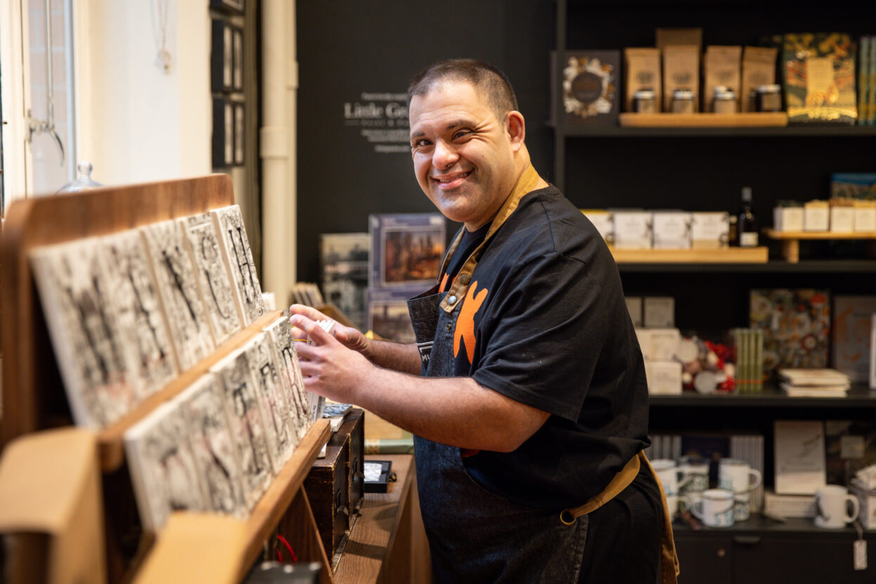 A man working in the Mcr Museum shop smiling at the camera.