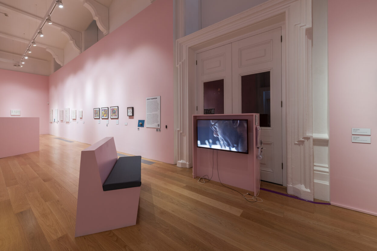 A gallery with pink walls and a bench positioned in front of a TV.