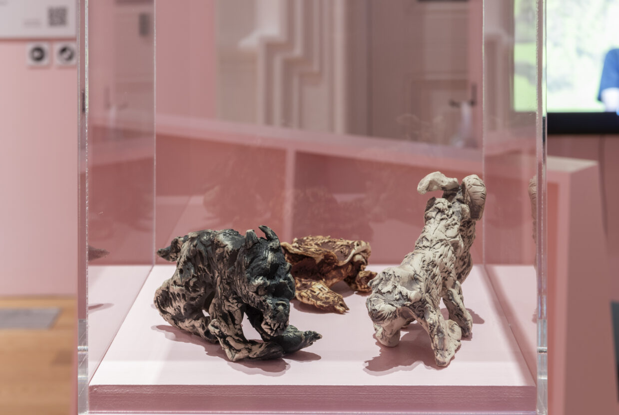 Three ceramic sculptures of animals in a glass case, with pink pedestal.