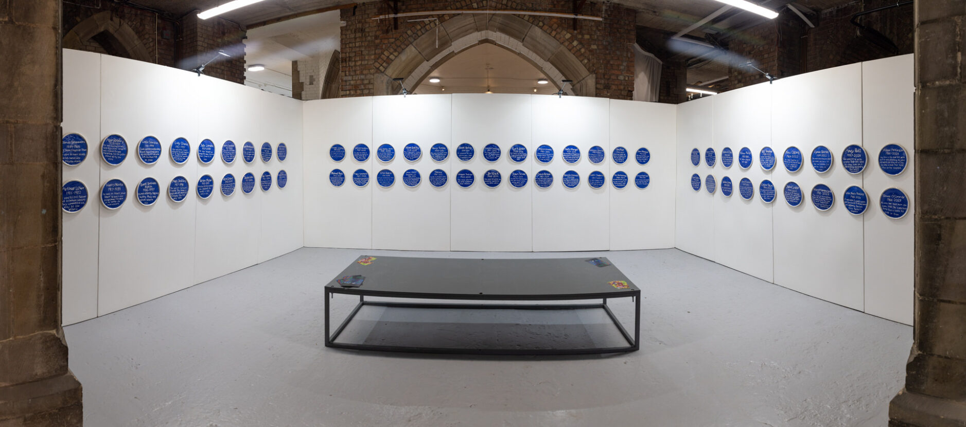 60 of Horace Lindezey's ceramic blue plaques displayed on white gallery walls.