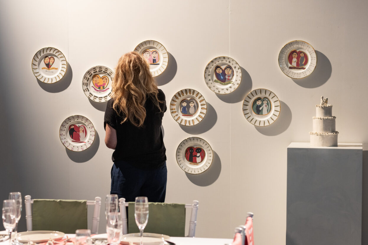A woman stood in front of ceramic plates displayed on a white gallery wall.