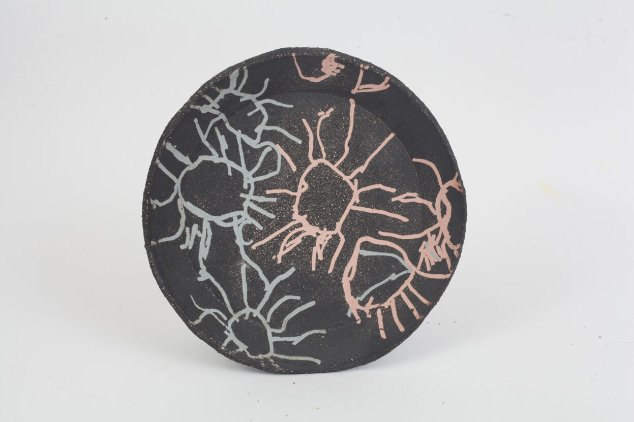 Black ceramic plate by Emma Horton with firework design inscribed in pink and blue.