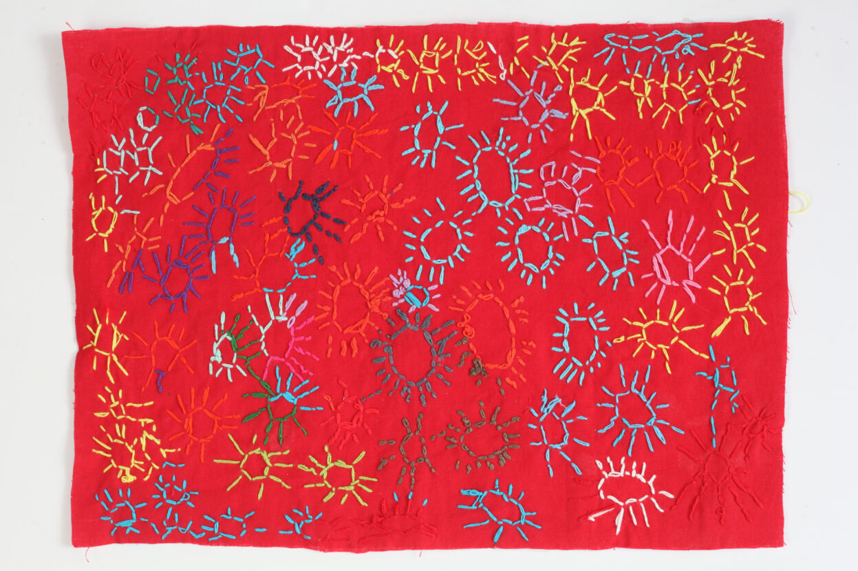 Firework design embroidered in to a piece of red textile by Emma Horton.