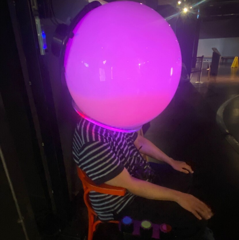 A person sat on a chair with a large pink light up bulb over their head.