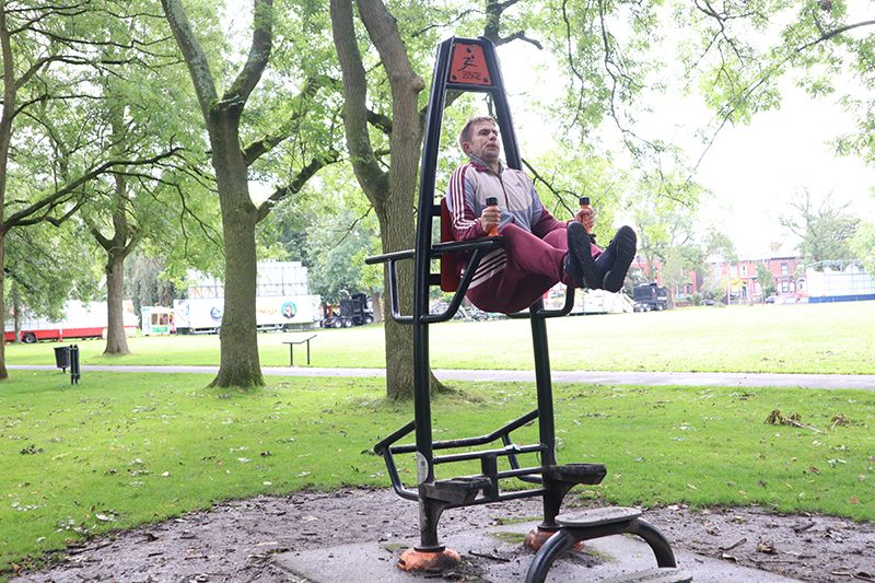 A young white man using exercise apparatus in a park.